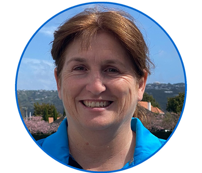 Smiling woman with brown hair in a blue shirt, outdoors with hills in the background.